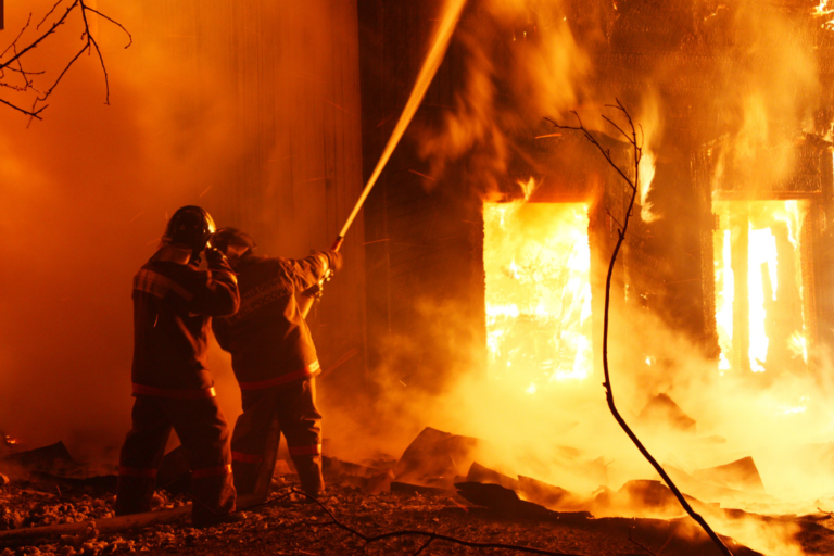 Pompiers combattant un incendie de maison avec des lances à incendie la nuit.